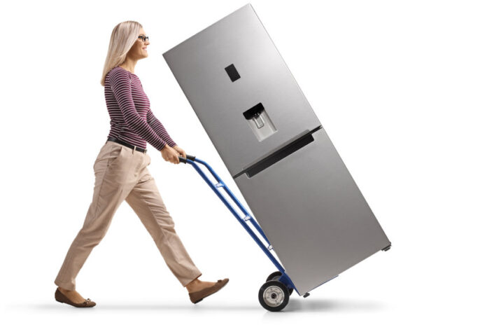Full length profile shot of a young woman pushing a hand-truck w